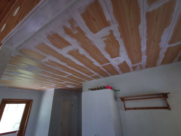 Innertak i en hall under renovering med delvis målad furupanel och en ommålad hatthylla på väggen.