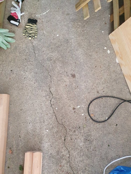 T-formad spricka i en grå betongplatta inne i ett garage, med verktyg och en kabel på golvet.