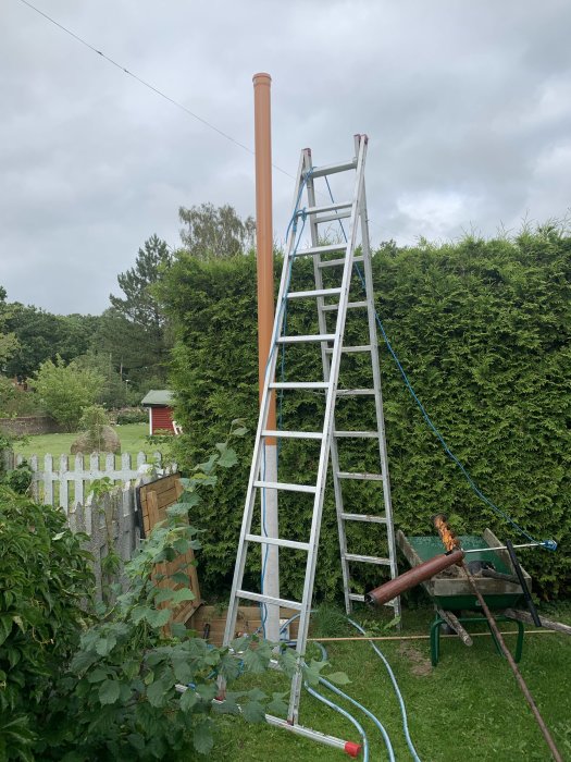 Bild av ett brunnsprojekt med en lång PVC-rör stående uppåt i en stege, omgiven av en trädgård och växtlighet.