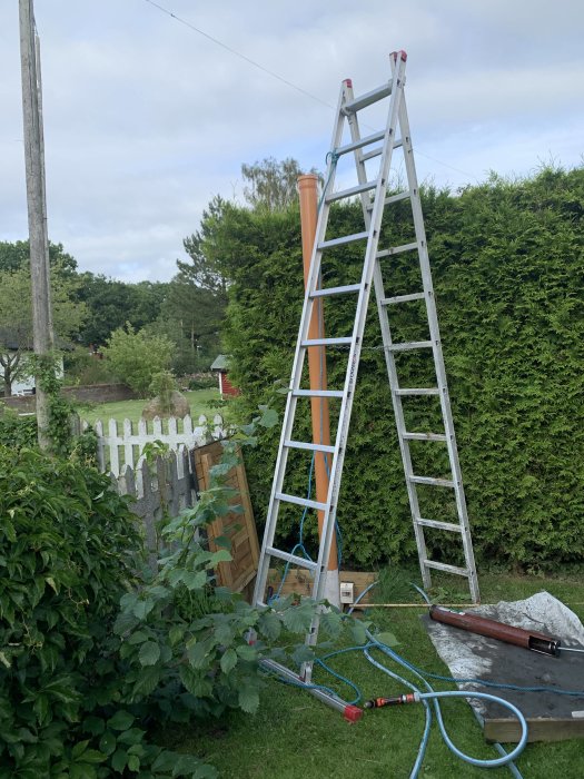 En trädgård med en stege som står bredvid ett oavkortat sexmetersrör och en kiespump på marken, redo för byggprojekt.