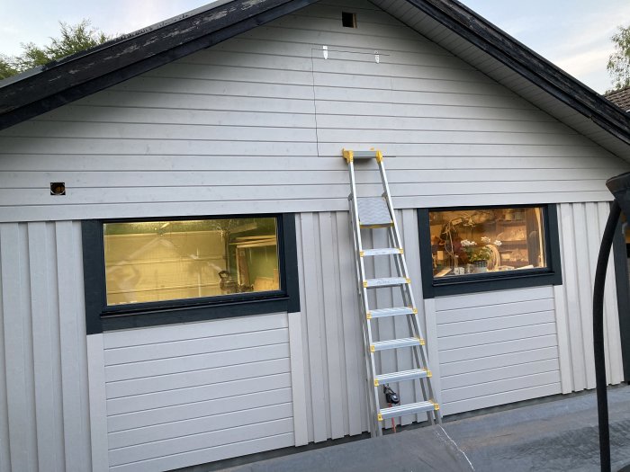 Husfasad med nyinstallerat foder runt ett fönster och en vindslucka, stege lutad mot väggen.