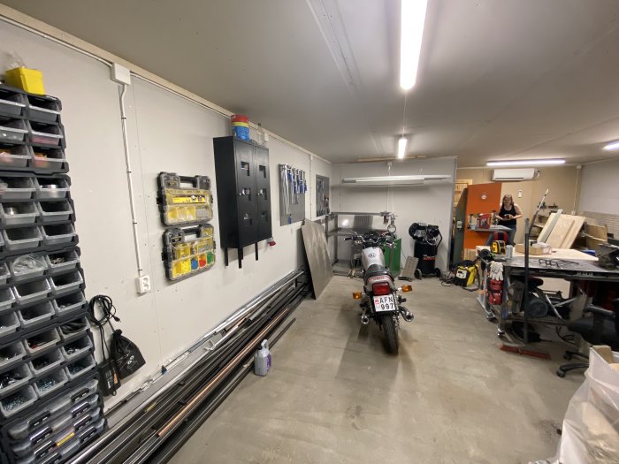 Omorganiserat garage med arbetsbänkar i mitten, verktygssystainers och motorcykel.