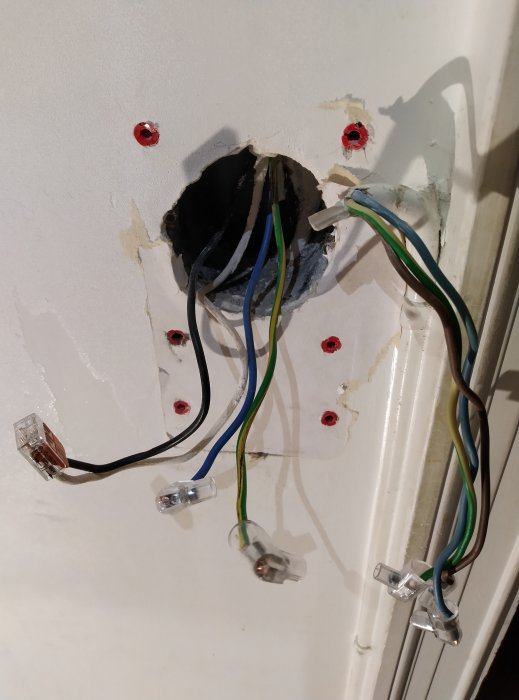 Elledningar med skruvklämmor i en vägg under renovering, med blå, grön/gul, svart och vit tråd.