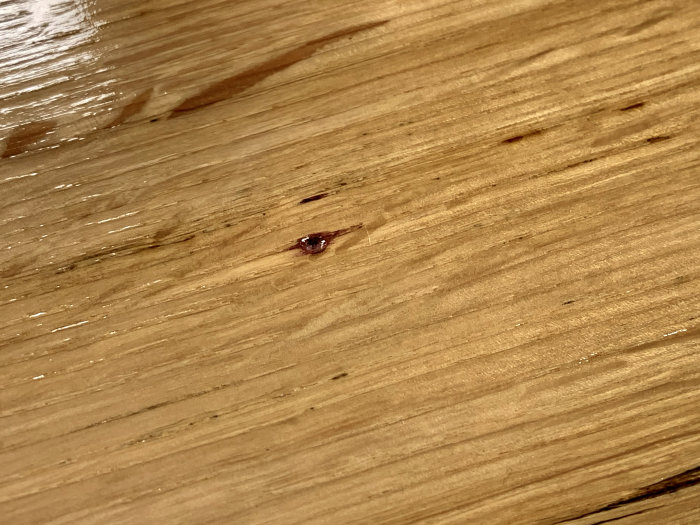 En närbild av en träbräda behandlad med olja där en droppe rödvin har missfärgat ytan och punkterat behandlingen.