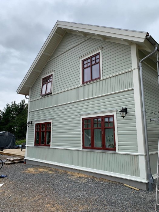 Ny målad fasad på lösvirkeshus med liggande panel och röda fönster, i ljusgrönt och vitt.