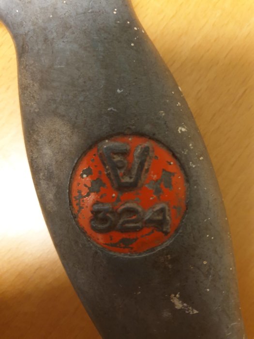 Närbild av ett verktygshandtag med ett slitet märke med bokstaven "V" och siffran "324" på en orange bakgrund.