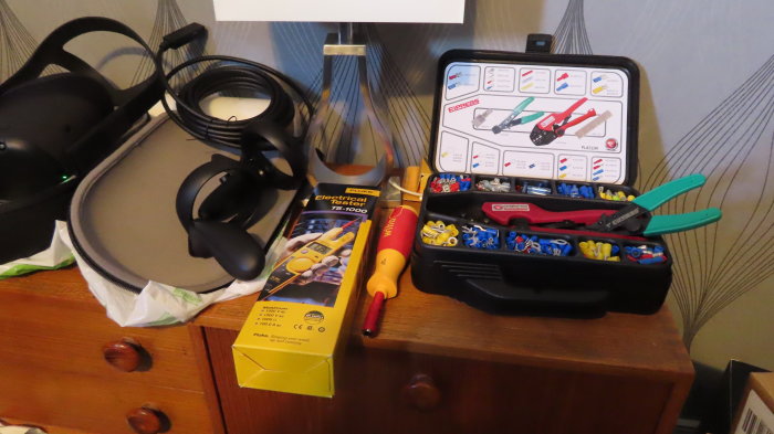 Elektrikerverktyg och tillbehör på ett bord, inklusive en multimeter, skruvmejslar och en verktygslåda med kontakter.