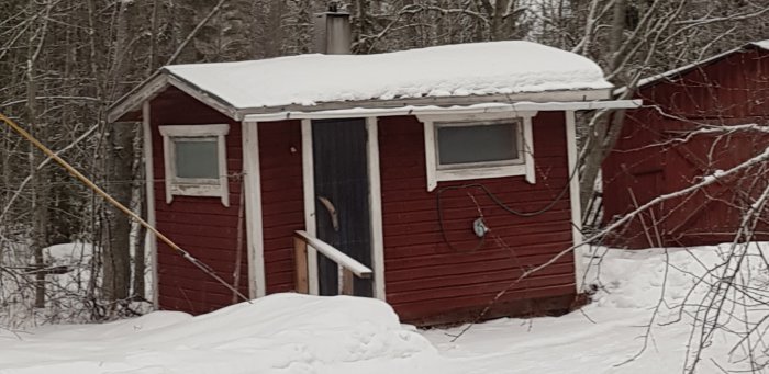 Röd bastustuga med snötäckt tak i vinterlandskap, Norra Karelen.