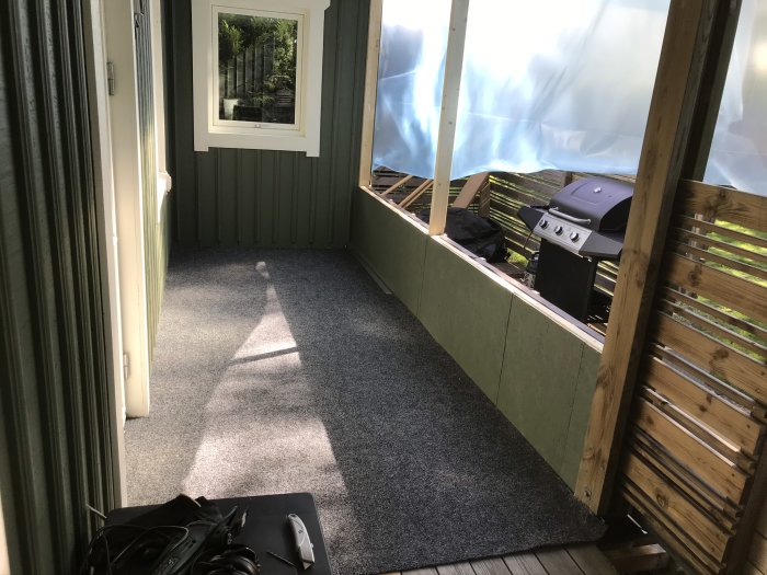 Inbyggd balkong med liggande träpanel och balkongmatta, naturligt ljus, grill och möbler under konstruktion.