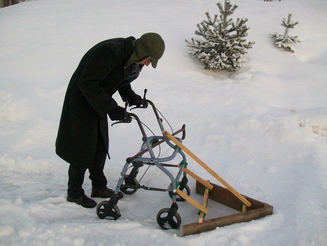 Person använder en rollator utrustad med en hemmagjord träsnösläde i snötäckt landskap.