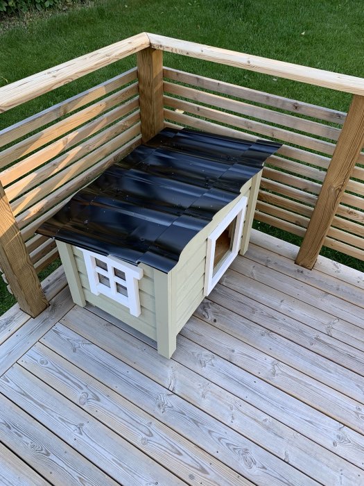 Ett litet katt hus i trä på en veranda, ofullständigt med plats för kylridå.