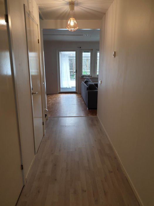 Hall med synliga vågräta ränder på innerväggen, lampan tänd och dörr öppen mot ett vardagsrum.