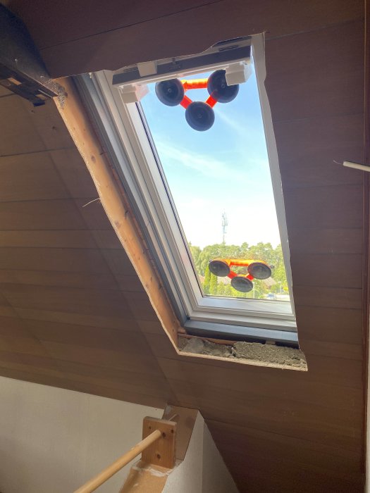 Nymonterat takfönster med utsikt mot himmel och reflekterande solskydd, sedd från ett inre trapphus.