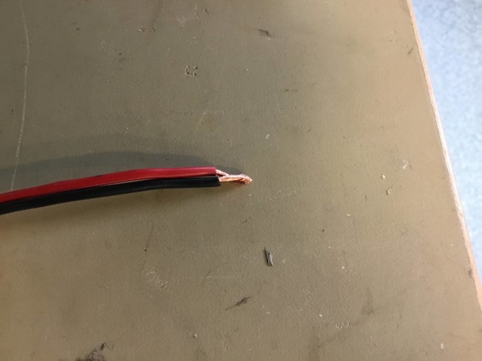 Röd och svart avskalad elkabel på beige yta med synliga koppartrådar.