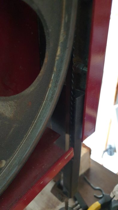 Delvis oskarp bild av nedre delen av en bandsåg med fokus på bandsågsbladet och dess stödstruktur.