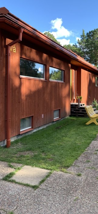 Nyinstallerat brunt stuprör på röd träfasad av hus, med grön gräsmatta och solig himmel i bakgrunden.