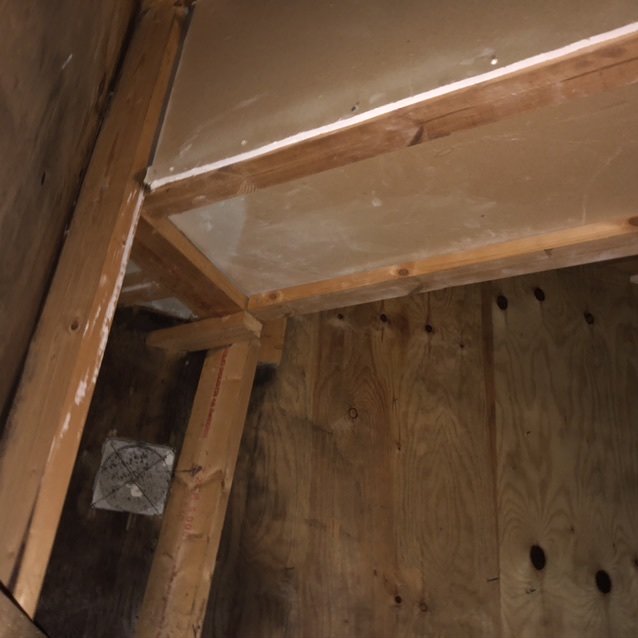 Puinen rakenne ullakolla, jossa on osittain rapistunut valkoinen levy.