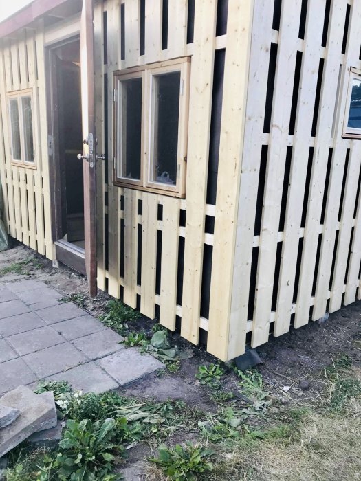 Nyoljad träpanel på hus, stor ytterdörr och långt fönster under installation.