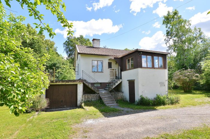 Villa från 1945 med brun och vit fasad, betongtrappa och vildvuxen trädgård.