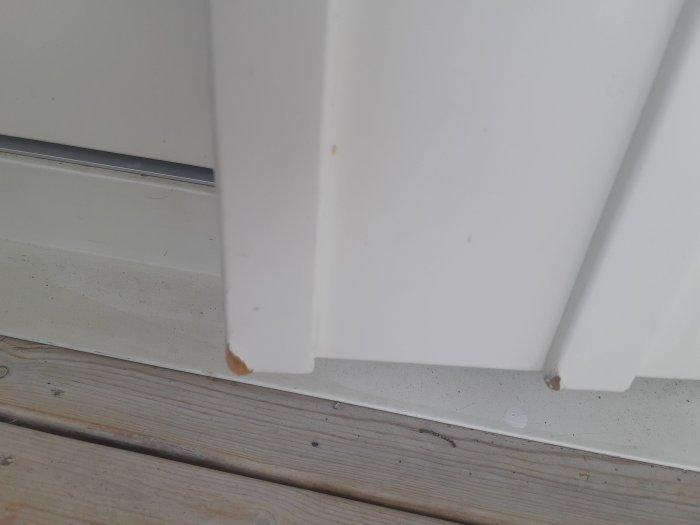 Närbild på vit ytterdörr med svullnad och avskalad färg på nedre hörnet.
