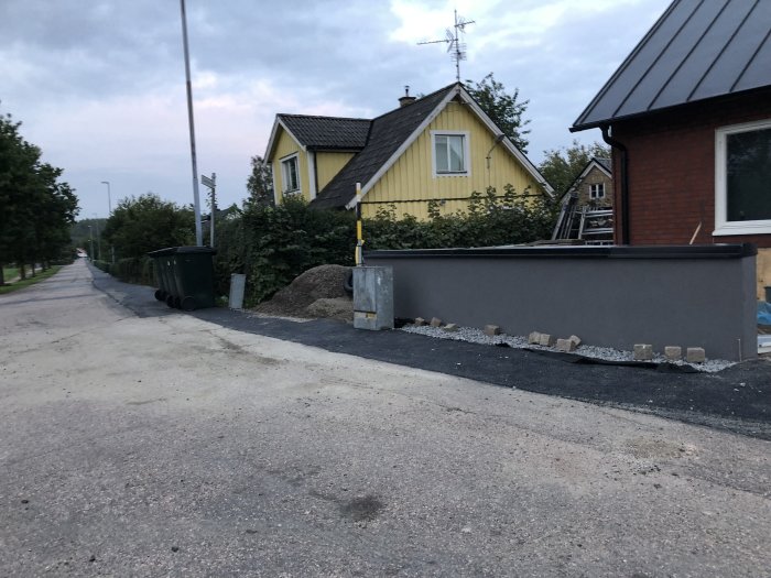 Nybyggd mur av skalblock som är putsade längs en gata med hus i bakgrunden.