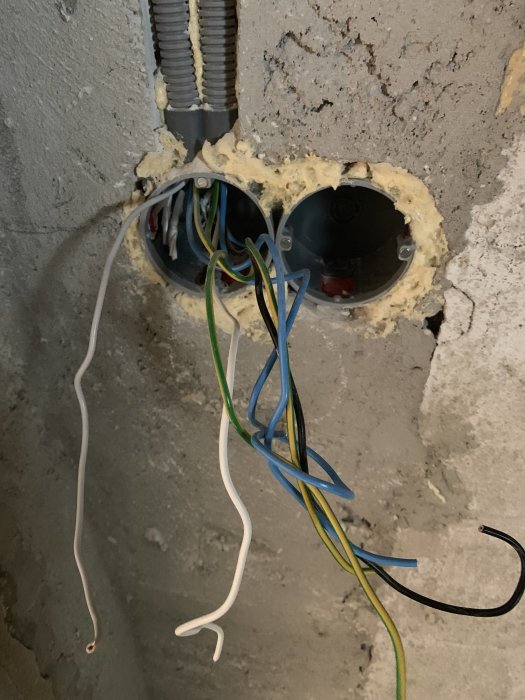 Elledningar med blå, svart och gulgrön ledare syns utsatta ur en vägg inför installation.