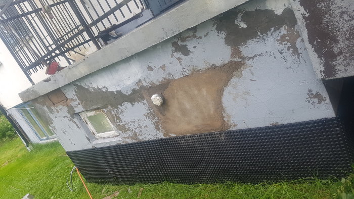 Husgrund med flagnad färg och en murad yta efter högtryckstvätt, samt en sida med platonmatta.