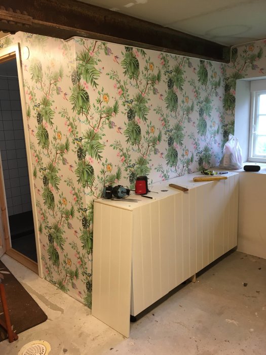 Renoverat badrum med blom- och fågelmönstrad tapet på väggarna och vit panel på halva väggen.