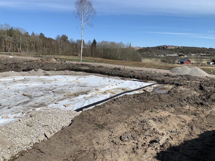 Husgrund och dränering under arbete med bergkross och grövre material i lantlig miljö.