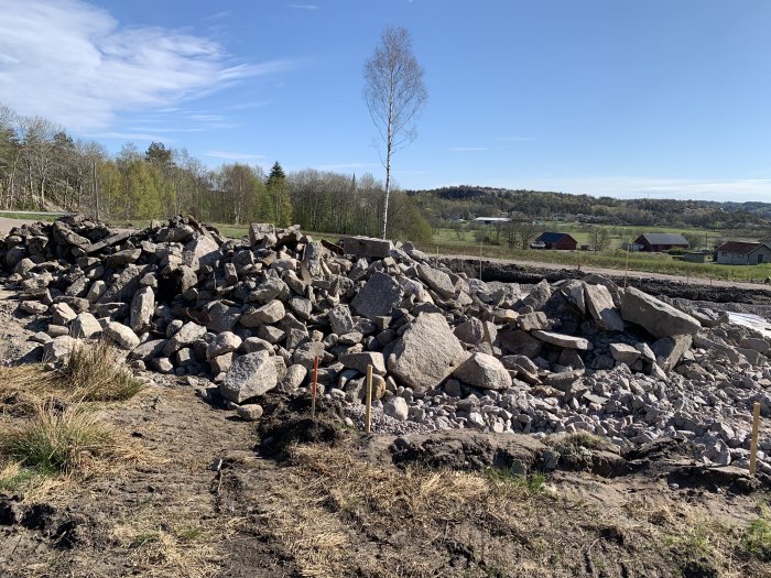 Husgrund med dränering under konstruktion, omgiven av bergkross och större stenar på en byggplats.