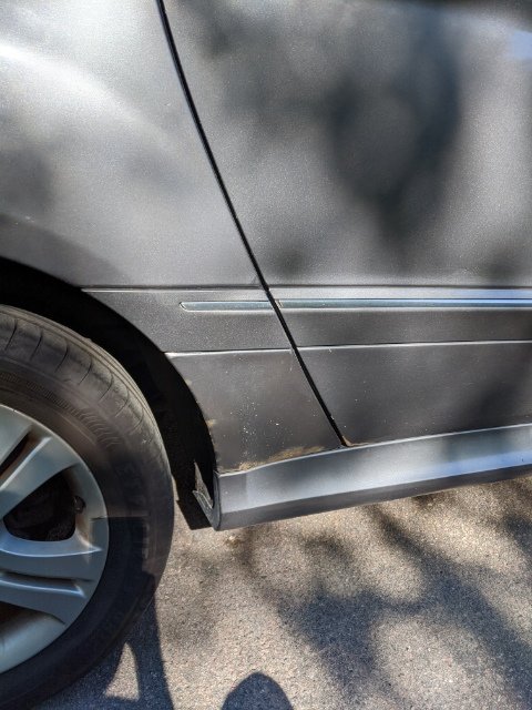 Rostskador längs nedre dörren på en grå Mercedes, synlig under reparationens klarlack.