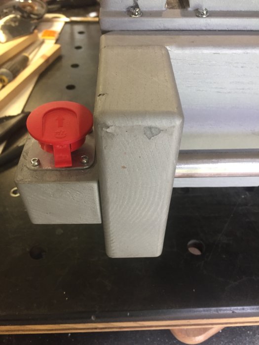 Monterad stor röd brytarknapp på grått sågstativ, med fokus på installationen och detaljer för användbarhet.