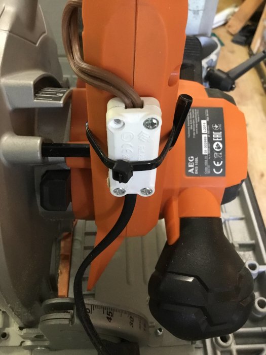 Monterad stor röd brytarknapp på såg med kopplingsdosa och kabelanslutning, detaljfokus på installation.