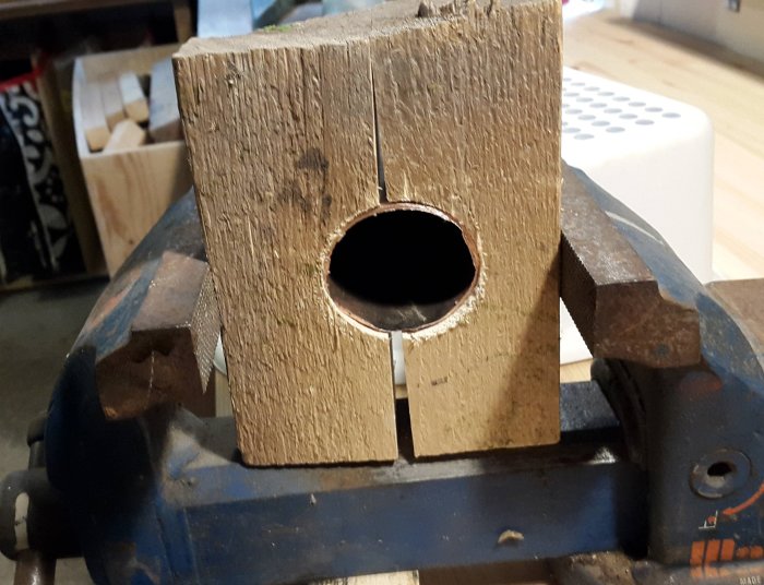 Wooden block with a circular hole clamped in a vise, used for shaping during a pole repair.