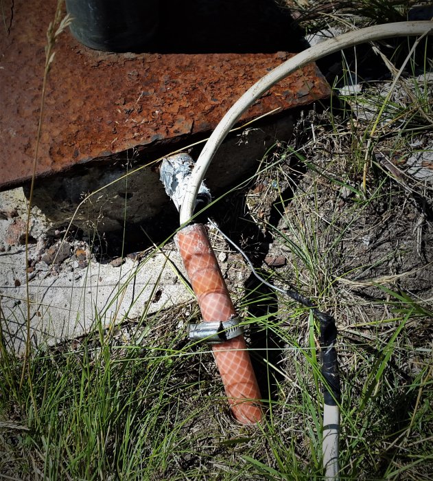 Close-up of a repaired pole on the ground, with soldered joint visible and cable connected. Rusty metal plate and grass surround the setup.