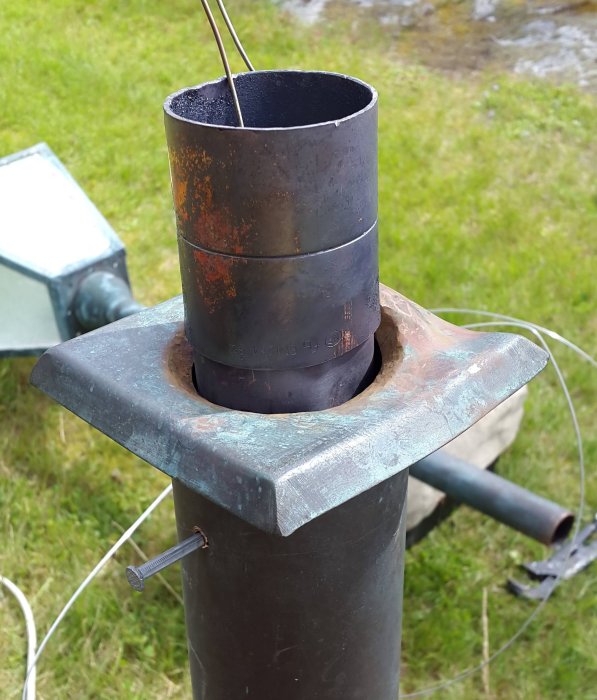 Close-up of a repaired and soldered post with inserted cable, showing metal join and surrounding tools. Grass background and electrical setup visible.