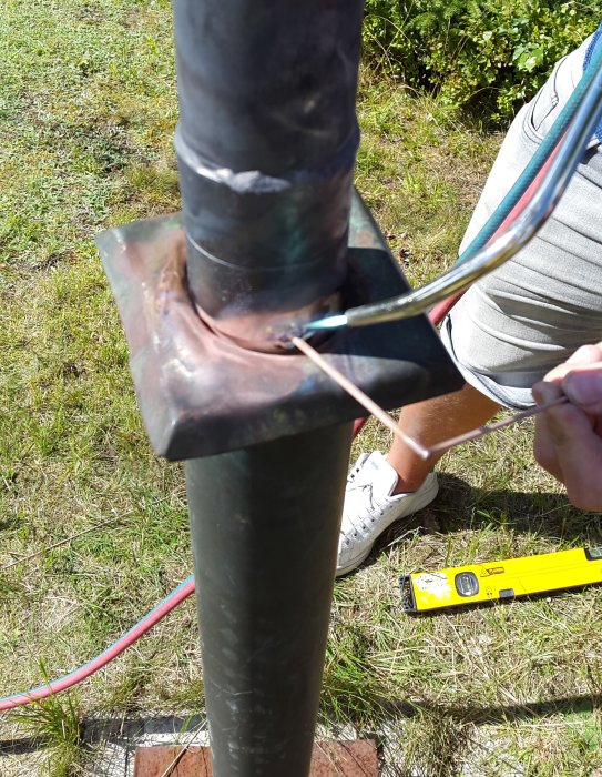 Close-up of a repaired pole with a soldered joint, held by a person outdoors, showing inserted cables and a tool for alignment.