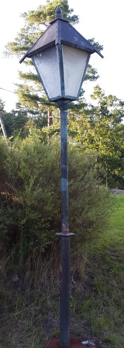 Restored lamp post with soldered joint, new wiring, and repaired top section, set outdoors against trees and bushes.