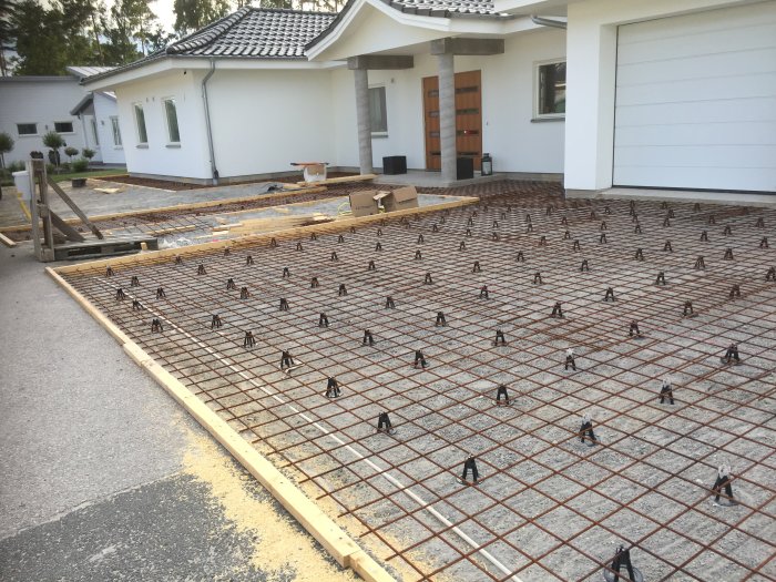 Armeringsnät för betonggjutning klar för 8mm mattor framför ett vitt hus med garage.