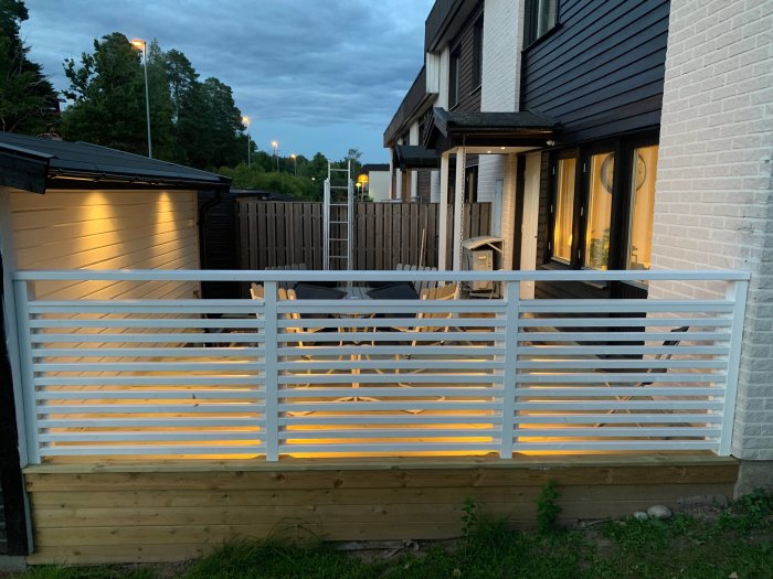 Oavslutad altan vid skymning med frästa utrymmen där elen döljs, vit brädstaket belysning, hus i bakgrunden.