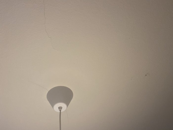 Krackelerat innertak från 50-talshus med synliga sprickor och en vägglampa, som illustrerar en fråga om renovering.