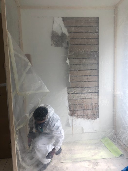 Person i skyddsutrustning tar bort en väggyta för dubbeldörr i sekelskifteshus, dammigt arbetsområde.