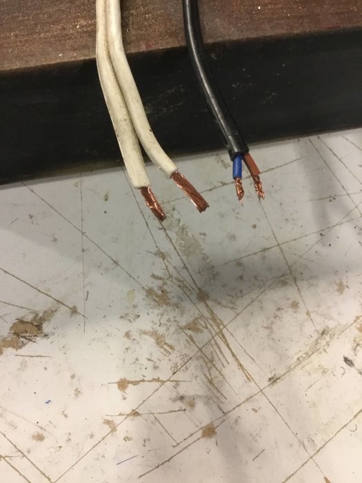 Kabeländar på en vit och svart elkabel, frilagda kopparkärnor mot en smutsig bakgrund.