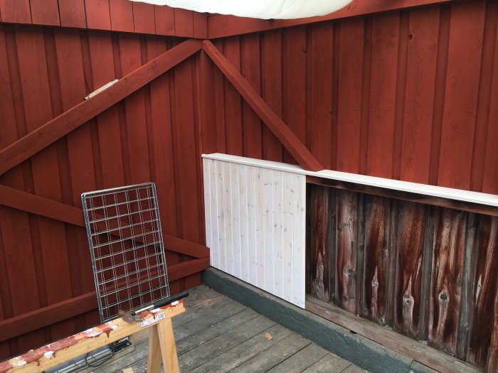 Hörn av ett uterum med faluröda väggar och nymålad vit panel, omgivet av renoveringsverktyg.