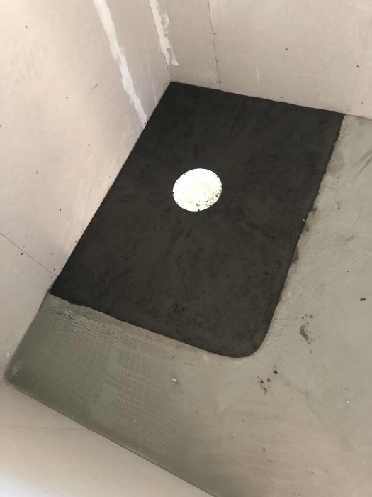 Nygipsade väggar och ett lokalt fall med golvbruk runt golvbrunn i en dusch under konstruktion.