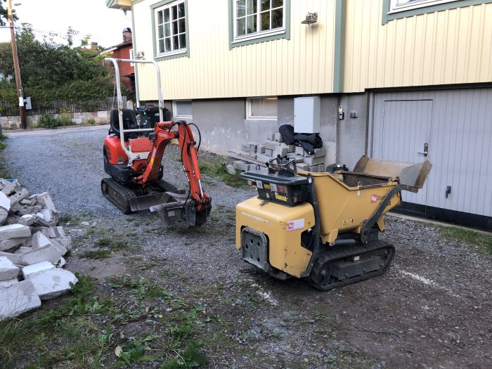 Minigrävare och minidumper vid byggprojekt, redo för grävarbete nära husfasad.