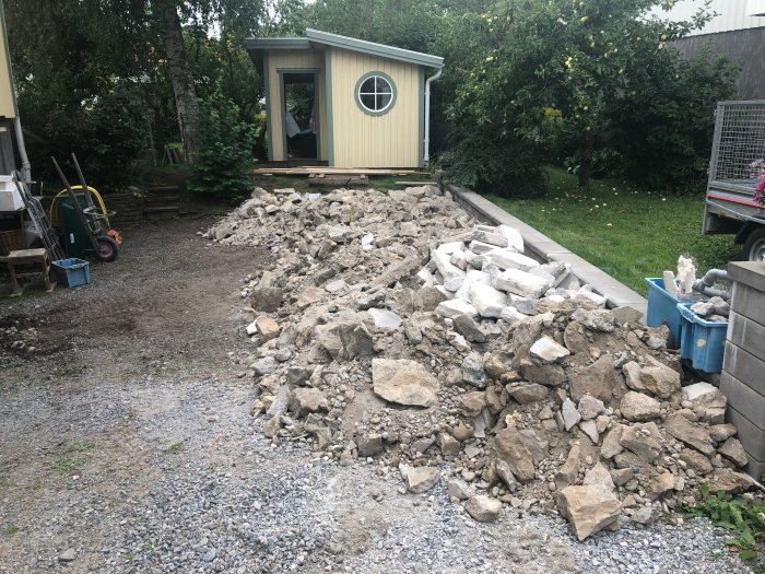 En uppbilad betongplatta och högar av grus och sten utanför ett hus under renovering.