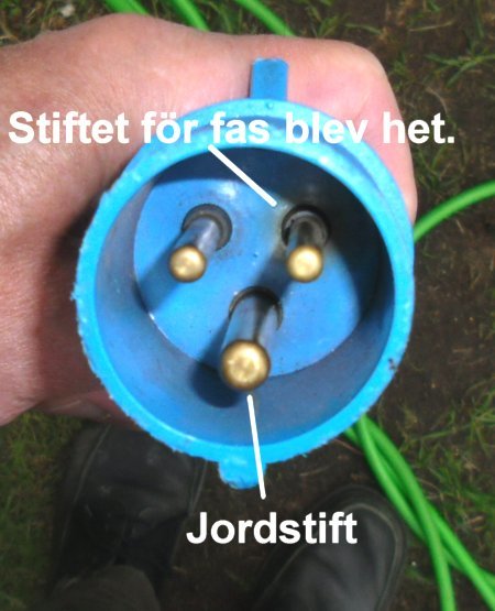 Blå CEE-husvagnsstickpropp med brunbränt område runt fas-stiftet och intakt jordstift, som hålls i en hand.