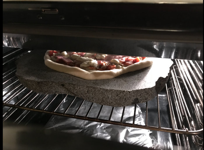 En ofärdig pizza på en pizzasten inne i en ugn.