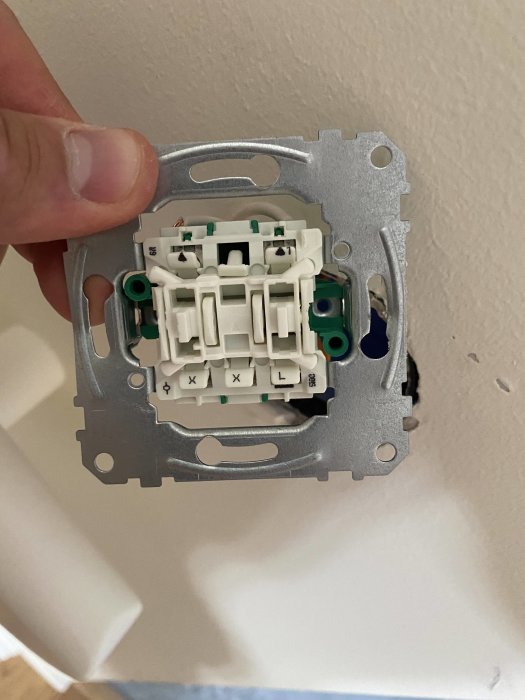 En hand håller en öppen ljusbrytare i väggen med synliga kablar och anslutningar.